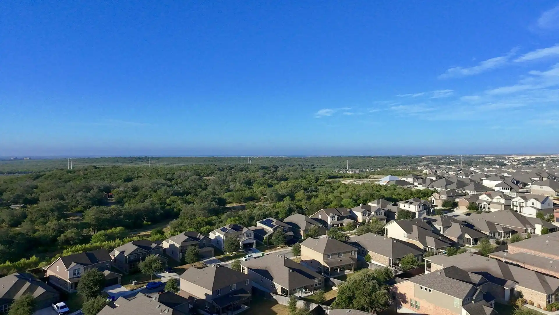 Aerial view of a Texas subdivision of shingle-roofed homes surrounded by live oak woodland