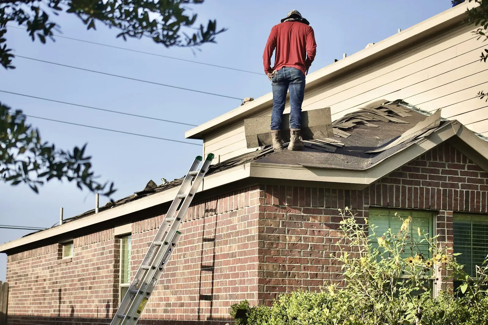 Roofer standing on a brick home during a tear-off, ladder against the wall