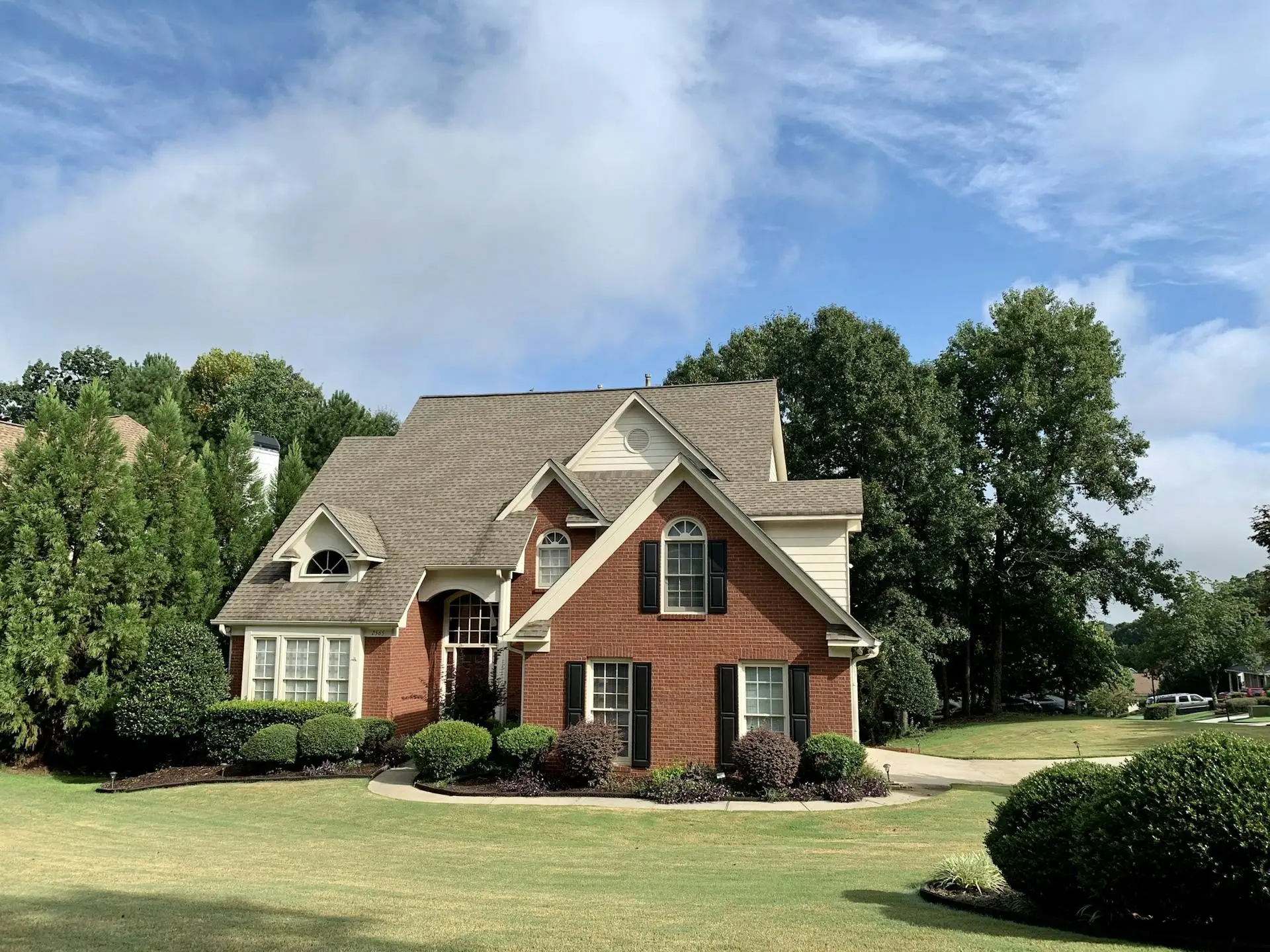 Two-story brick and stone house with a new architectural shingle roof under mature trees