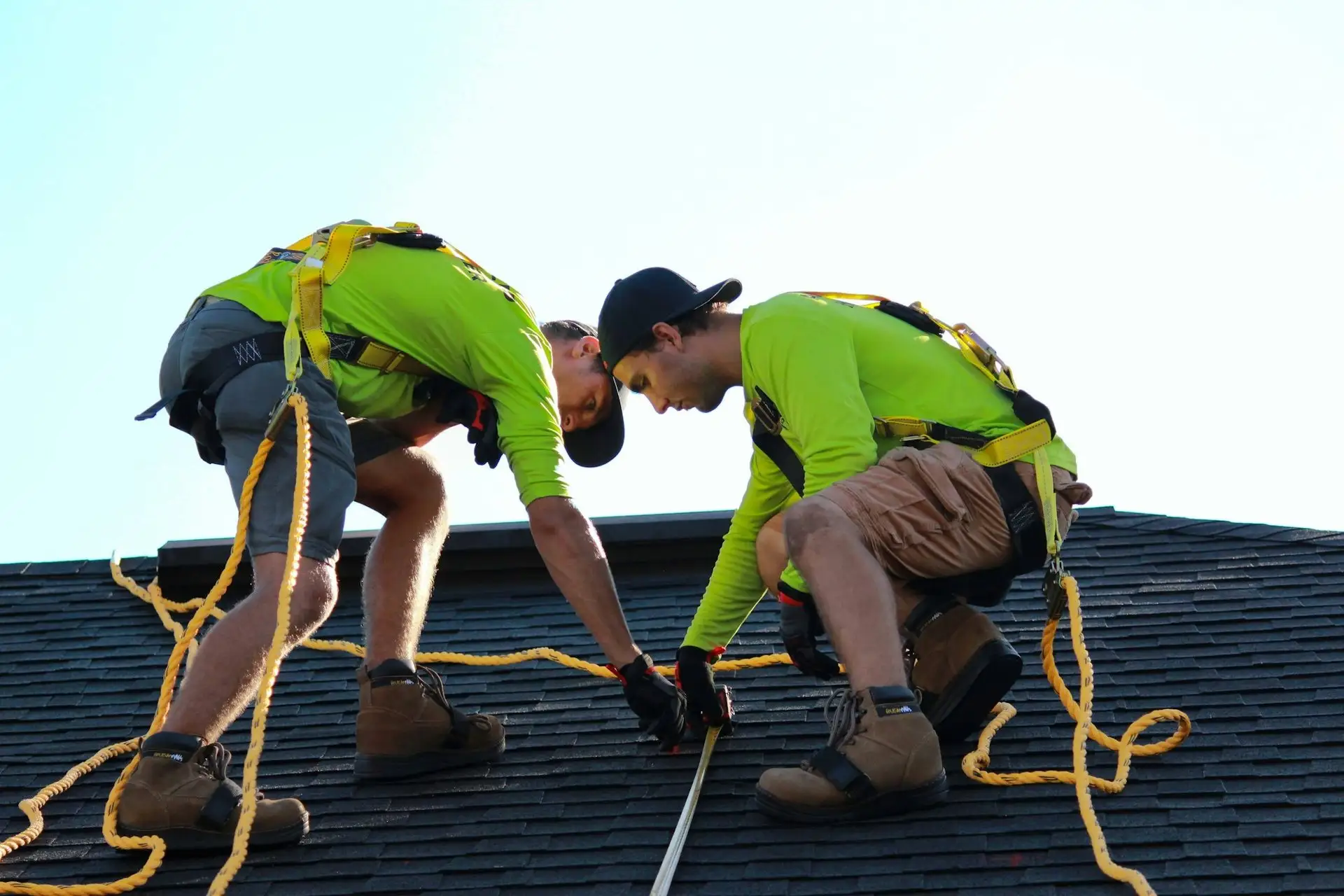 Two roofers kneeling on a shingle roof, lining up the next course