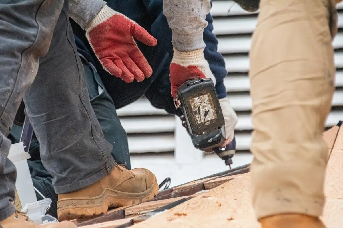 Roofer's boots and gloved hands fastening new plywood decking with a drill