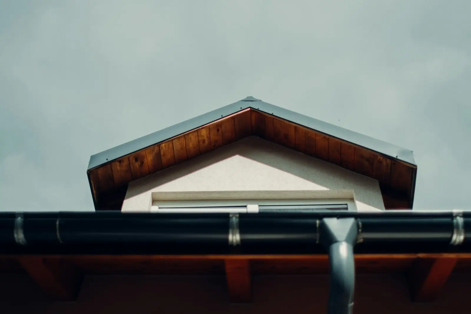 New dark gutter and downspout along a roof eave under a wood soffit