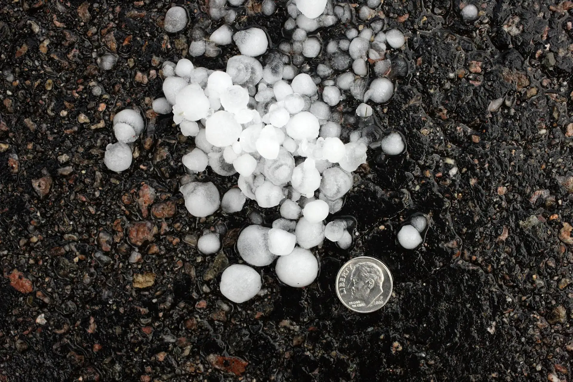 Pile of hailstones on dark asphalt next to a dime for scale
