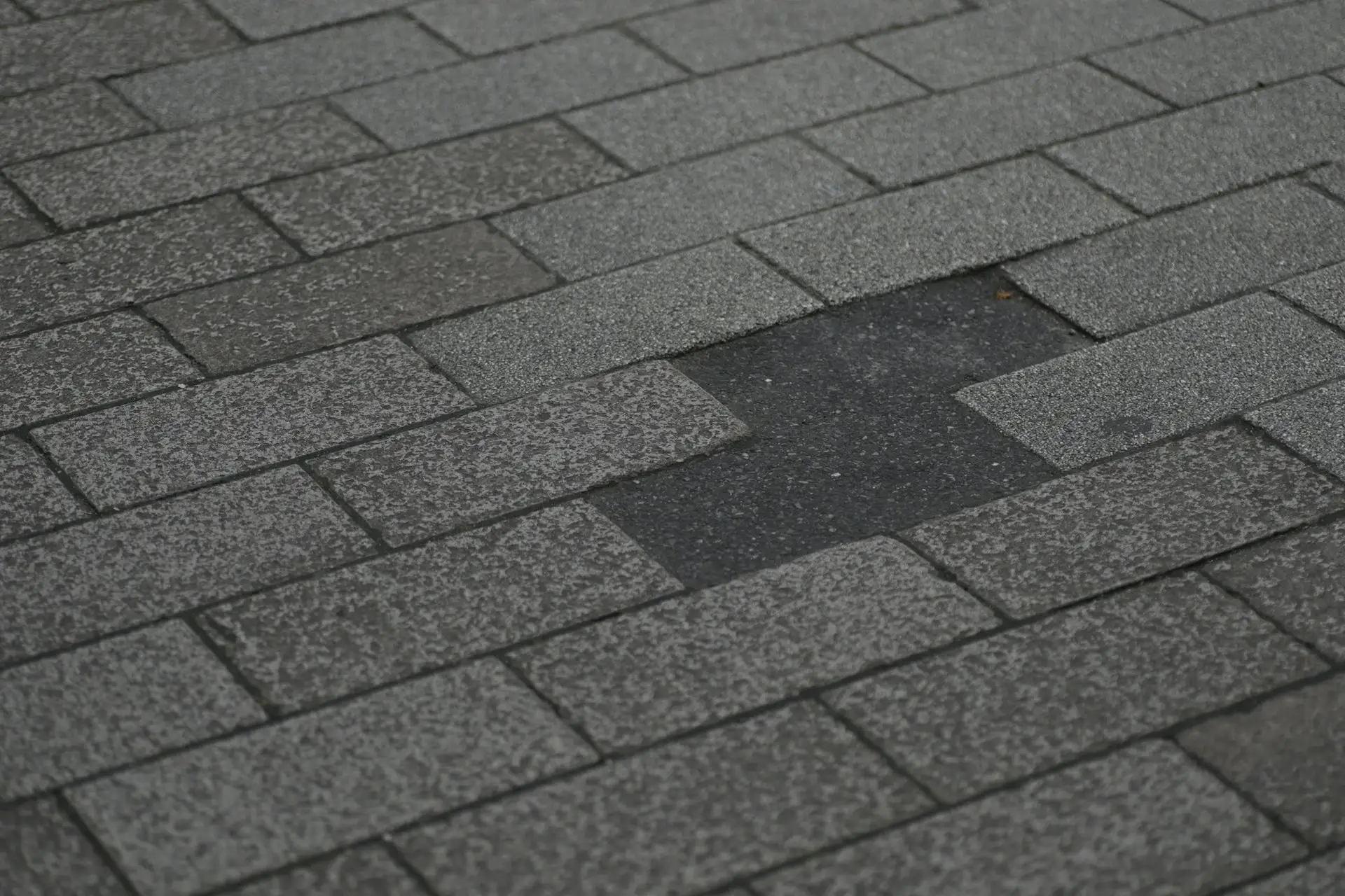 Asphalt shingle roof with a patch of shingles missing and the darker layer showing through