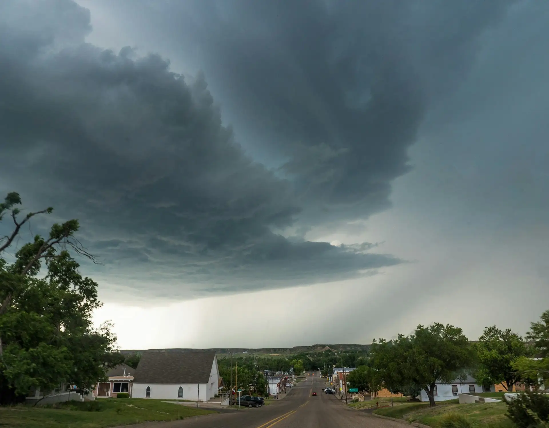 Dark rotating storm cloud building over rooftops and trees